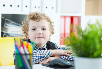 Little boy looking at camera sitting at computer in office