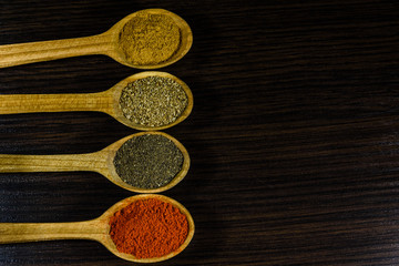 Spoons with the different spices on dark wooden table. Top view