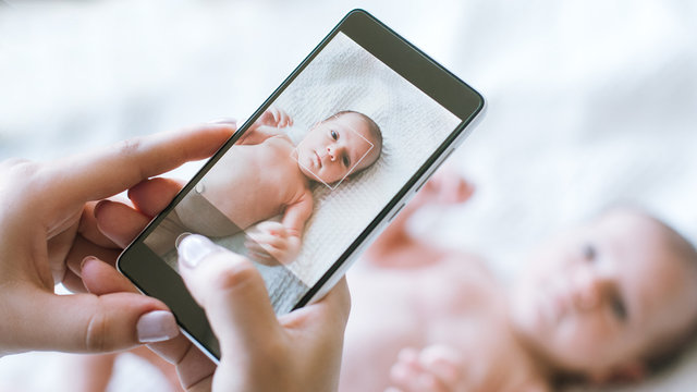 mother takes a photo of her newborn baby on a smartphone. family memories.