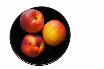 Three yellow red peach fruits in black bowl isolated