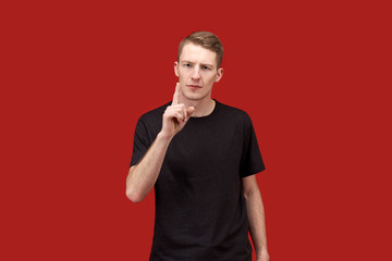 a young handsome guy with short brown hair in a black t-shirt with a serious expression on his face warningly shows the index finger and frowns.