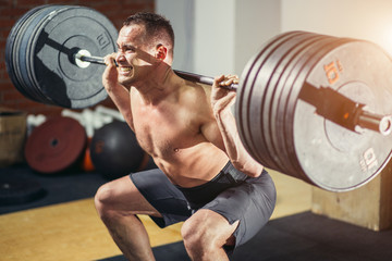 Muscular man training squats with barbells on shoulders.