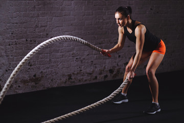 Athletic woman doing battle rope exercises at gym