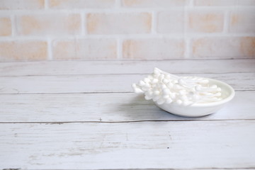 Selective focus of white cotton buds or cotton swab on a small white plate on wooden background with copy space for text.