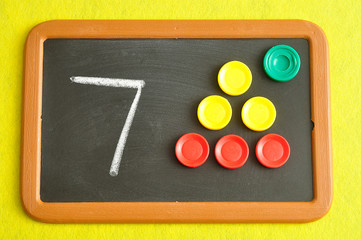 A number seven written on a black board with the same quantity showed by colorful round tokens