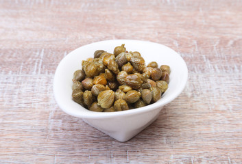 bowl with fresh capers on wooden table