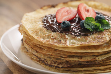 stack of crepes with berries and dark chocolate poured on top