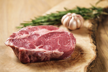 fresh raw rib eye steak on wood board on kitchen table