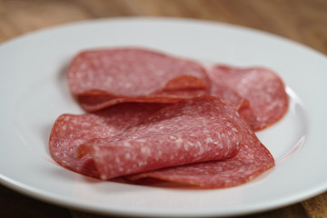 sliced salami on white plate on wood table