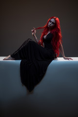 Beautiful red haired woman in black dress posing in gothic entourage