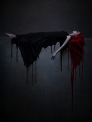 Beautiful red haired woman in black dress and blood lying on the stone.