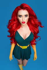 Beautiful woman in green superhero costume posing at camera on blue background