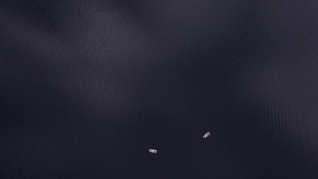 Shooting from helicopter flying over a pond, sea, ocean. Fishermen are sitting in fishing boats in the middle of the sea in Norway, Europe. Smooth surface of the sea with a ripple on the water