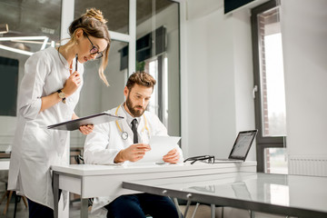 Senior doctor with young female assistant working with medical documents at the white office interior