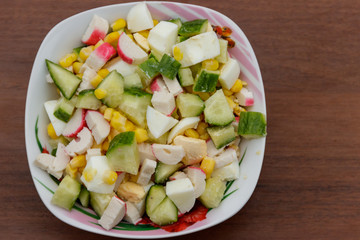 Salad with crab sticks, sweet corn, cucumber and eggs on wooden table