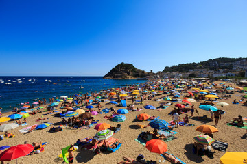 View of the beach full of people in the month of August, with the castle in the background, in Tossa de Mar, Girona, Spain