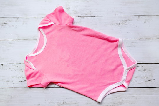 Top view of pink baby romper on white wooden background. Copy space for text or graphic.