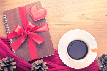 Obraz na płótnie Canvas Valentine or love theme, felt heart and Made With Love button sitting on notebook wrapped in red ribbon with cup of hot coffee or tea on wooden table