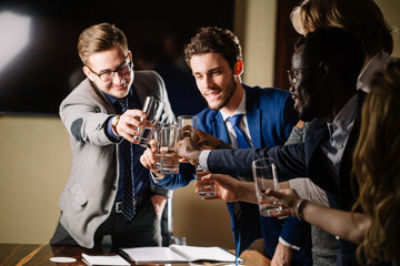 Successful business people are clinking glasses of champagne and smiling while celebrating in meeting