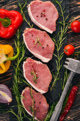 Beef steak with fresh vegetables and rosemary and spices on a black wooden background. Top view. Free space for text.