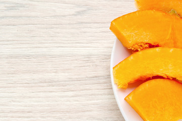 Pumpkin pieces on a white plate, on a wooden base, ready for cooking