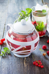 Hot fruit berry tea with mint, red currant and red raspberries on a wooden kitchen table.