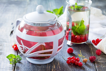 Hot fruit berry tea with mint, red currant and red raspberries on a wooden kitchen table.