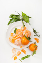 Fototapeta na wymiar Peeled tangerines and peel with leaves on white background