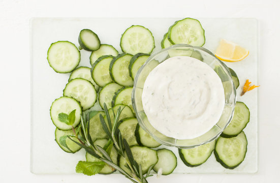 Cut young cucumbers and sour cream on a white background