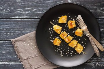 Fried bananas on a skewer are sprinkled with sesame seeds served on a black plate.