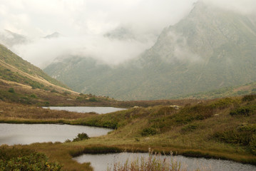 three strange round small karst lakes on a scenic mountain pass with a cloud covered mountain ridge...