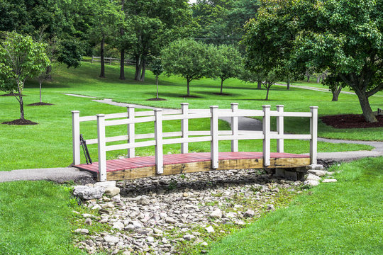 Exterior daytime stock photo of red and white wooden bridge spanning dry creek bed full of rock and brookstone at Green Lake in Orchard Park New York Erie County