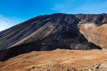 An uphill view of the colourful Teide volcano in Teide National Park, Tenerife, Canary Islands. Pictured in the distance is a cablecar leading up to the 3718 m Teide peak, the tallest peak in Spain.