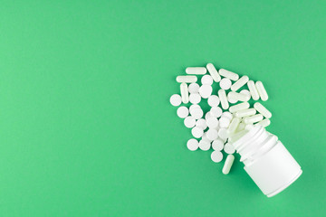 Close up white pill bottle with spilled out pills and capsules on jade green background with copy space. Focus on foreground, soft bokeh. Pharmacy drugstore concept. Top view