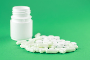 Close up white pill bottle with spilled out pills and capsules on jade green background with copy space. Focus on foreground, soft bokeh. Pharmacy drugstore concept