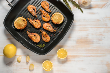 Grilled shrimps on a grill frying pan with lemon, paprika, spices and herbs. Wooden background.