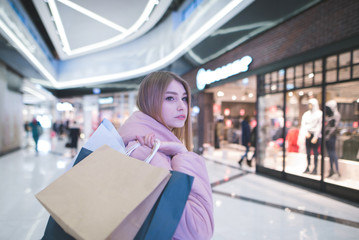 A sweet blonde with shopping bags in the yoke goes to the mall and looks to the side. Shopping concept.