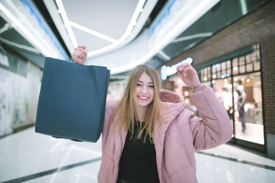 A smiling blonde girl raised shopping bags up while shopping in the mall. Shopping concept.