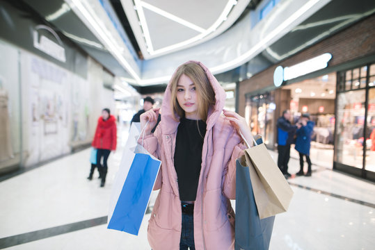 A pretty girl in a pink smoker stands in a mall against the backdrop of shops and people. Shopping concept.