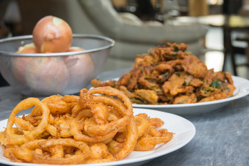 Onion ring in white dish with fried various vegetables on table