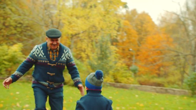 Little boys are playing with their grandfather with fallen leaves in the autumn park