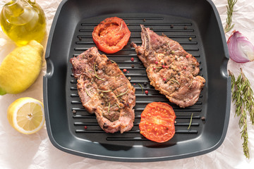 Grilled steak on grill pan with tomatoes and lemon on white background