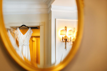 Elegant wedding dress hanging on the door and reflecting in the mirror