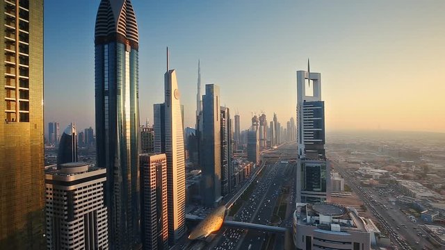 Dubai skyscrapers at sunset. Scenic aerial view over famous highway with fast moving traffic and financial center towers.