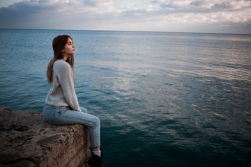 the girl is sitting on the pier near the sea