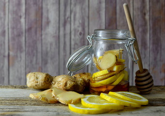 Closeup image of ingredients for natural cold or flu remedy includes ginger, honey in a jar, a honey drizzler and lemon on a wooden background.