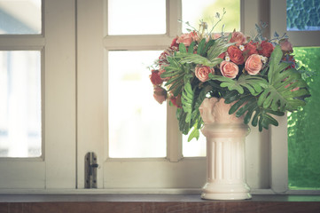 Artificial flowers in vase at window.