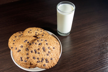 Chocolate chip cookies and glass of milk on wooden table