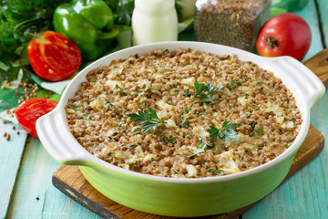 Fish casserole with buckwheat and various greens and vegetables on a kitchen wooden table.