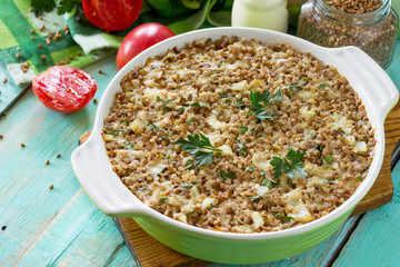 Fish casserole with buckwheat and various greens and vegetables on a kitchen wooden table.